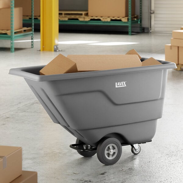 A gray Lavex tilt truck or trash cart with a 0.5 cubic yard capacity, shown holding cardboard boxes in a warehouse setting.