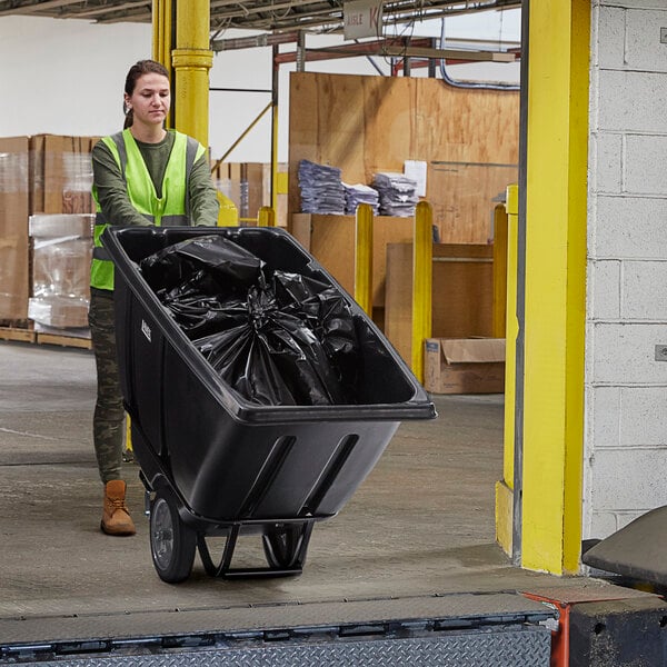 A woman in a safety vest pushing a black Lavex heavy-duty tilt truck.