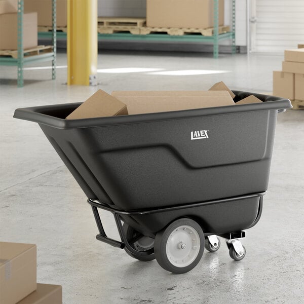 A black heavy-duty tilt truck or trash cart with a 0.5 cubic yard capacity, shown holding cardboard boxes in a warehouse setting.