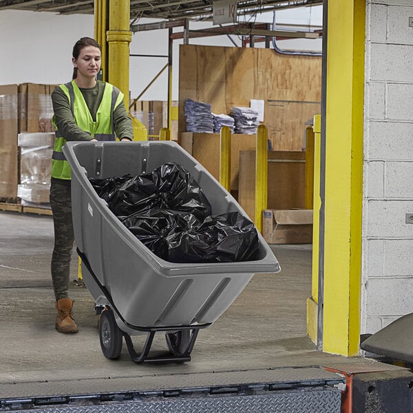 A woman in a safety vest pushing a grey Lavex tilt truck full of black garbage bags.