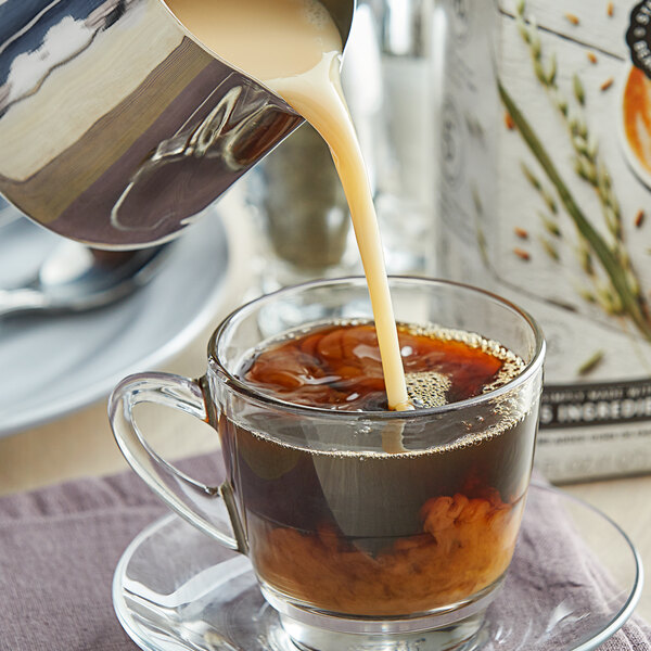 A hand pours Elmhurst Barista Oat Milk into a glass of coffee.
