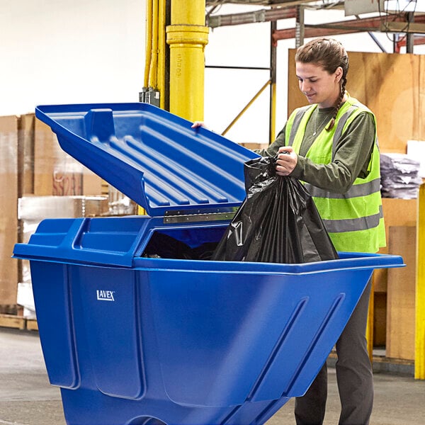 A woman putting a black bag in a blue Lavex tilt truck lid.