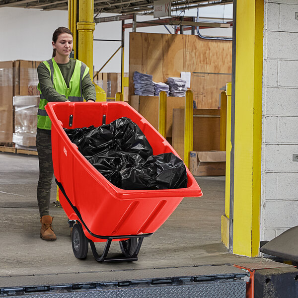 A woman in a green vest pushing a Lavex red heavy-duty tilt truck.