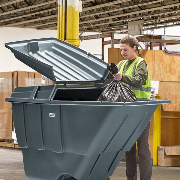 A woman placing a garbage bag into a Lavex gray tilt truck lid.