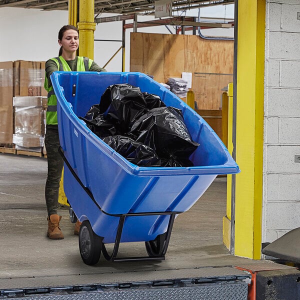 A woman pushing a Lavex blue tilt truck full of garbage.
