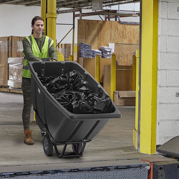 A woman pushing a black Lavex Heavy-Duty Tilt Truck full of garbage.