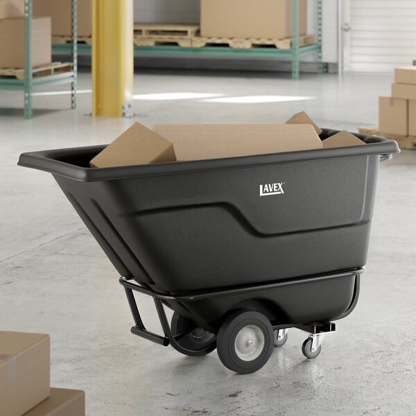 A black heavy-duty tilt truck or trash cart with a 0.5 cubic yard capacity, shown holding cardboard boxes in a warehouse setting.