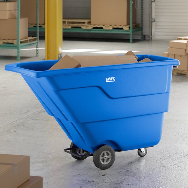 A blue Lavex 1 cubic yard tilt truck or trash cart with a 600 lb. capacity, shown in a warehouse setting with cardboard boxes inside.