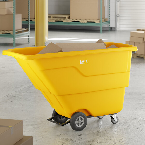 A yellow Lavex 1 cubic yard light-duty tilt truck or trash cart with an 850 lb. capacity, shown holding cardboard boxes in a warehouse setting.