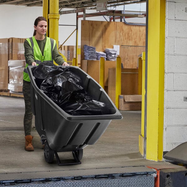 A woman in a green vest pushing a Lavex black garbage cart.