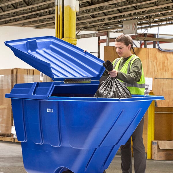 A woman in a safety vest holding a black bag is putting it in a blue Lavex tilt truck.