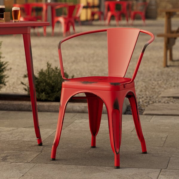 A red Lancaster Table & Seating outdoor metal arm chair on a stone patio.