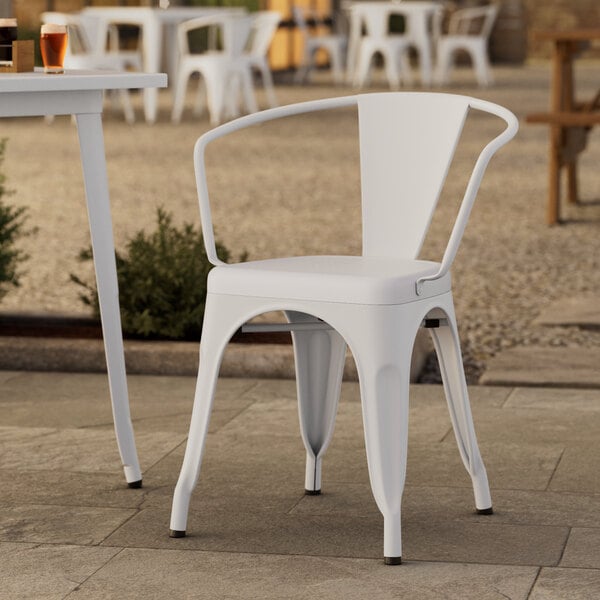 A white Lancaster Table & Seating outdoor arm chair on a stone patio.