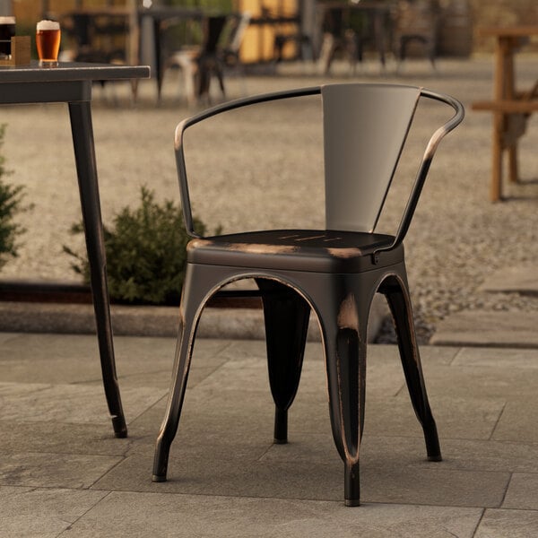 A Lancaster Table & Seating Distressed Copper outdoor arm chair on a stone patio.