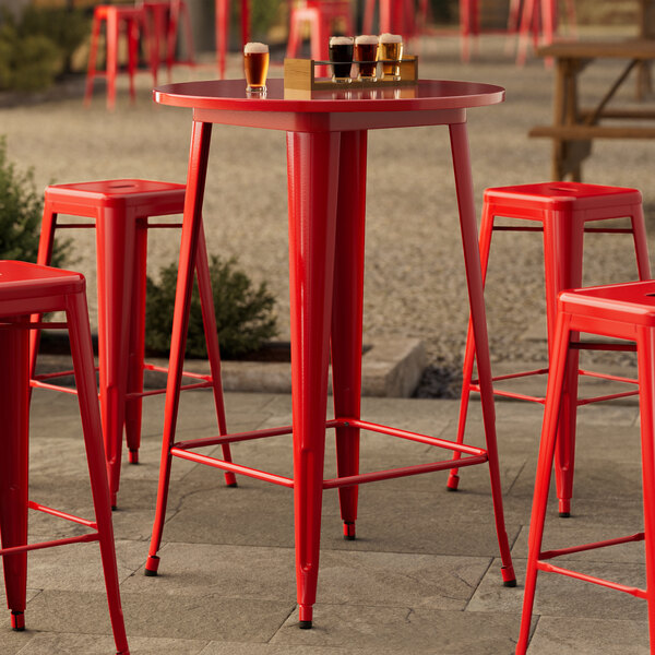 A Lancaster Table & Seating Ruby Red Bar Height Outdoor Table with red chairs on a concrete patio.