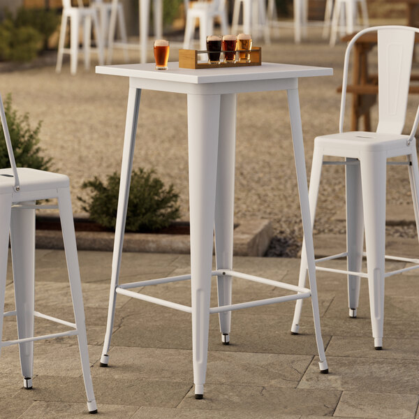 A Lancaster Table & Seating pearl white metal bar table with chairs on a patio.