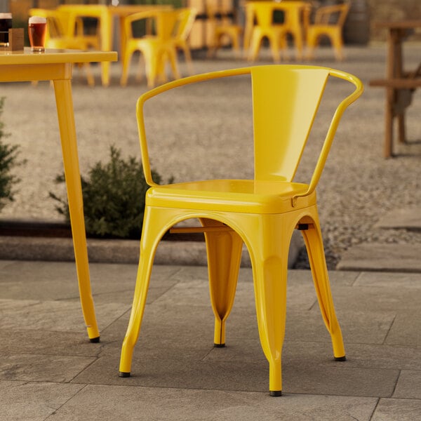 A yellow Lancaster Table & Seating outdoor arm chair on a stone patio next to a table.