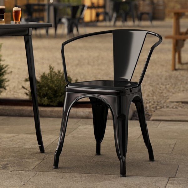 A Lancaster Table & Seating black metal outdoor arm chair on a stone patio.