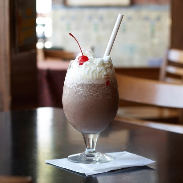 A white Aardvark paper straw in a glass of chocolate milkshake with whipped cream and a cherry.