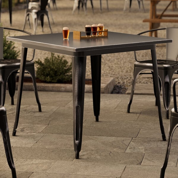 A Lancaster Table & Seating distressed onyx black outdoor table with glasses of beer on it.