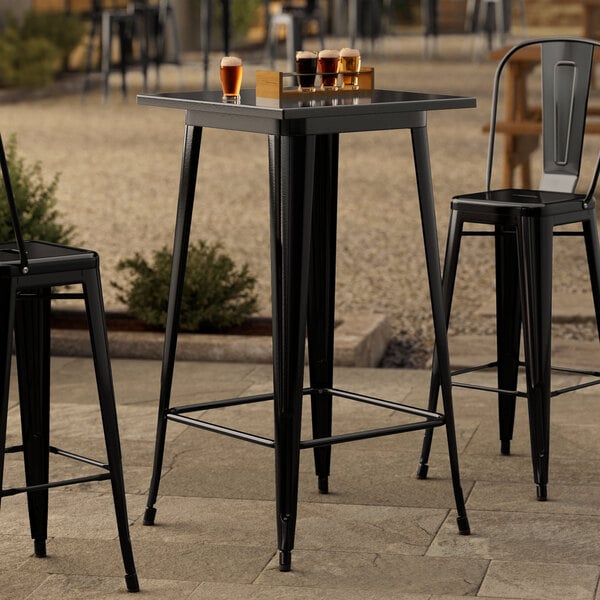 A Lancaster Table & Seating onyx black bar height table with black chairs on a stone patio.