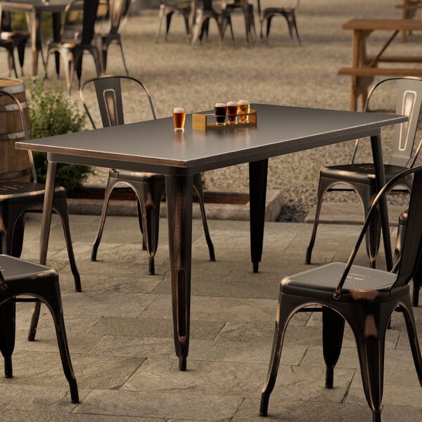 A Lancaster Table & Seating distressed copper table and chairs on an outdoor patio.