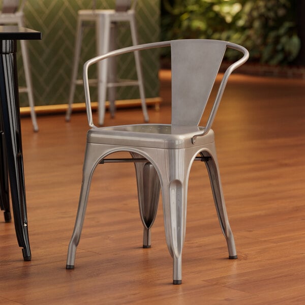 A Lancaster Table & Seating silver metal arm chair on a wood floor.