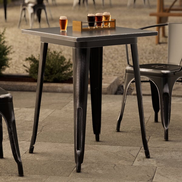 A Lancaster Table & Seating Alloy Series distressed onyx black table with drinks on it outdoors.