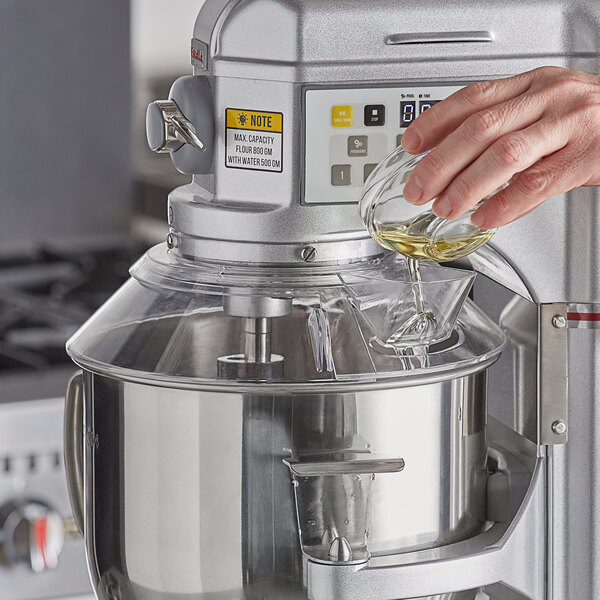 A person pouring liquid into a mixer with a bowl guard.