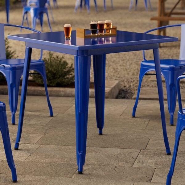 A Lancaster Table & Seating blue metal table with glasses of beer on it.