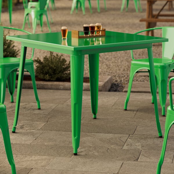 A green table with four chairs on a stone patio.