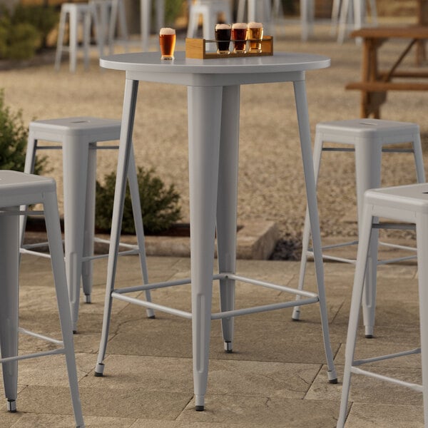 A Lancaster Table & Seating bar height outdoor table with several bar stools around it.