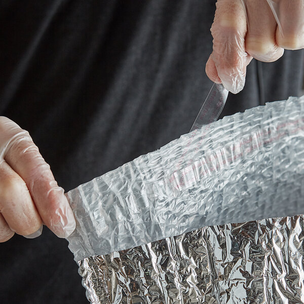 A person in plastic gloves using a Lavex insulated box liner to wrap a plastic bag with red text.