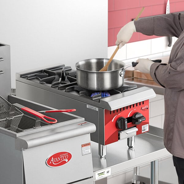 An Avantco Chef Series countertop gas range with two silver pots on burners, one with a wooden spoon in it.