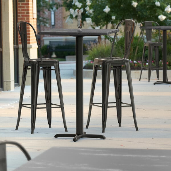 A Lancaster Table & Seating bar height table with a cross base plate and chairs on a patio.