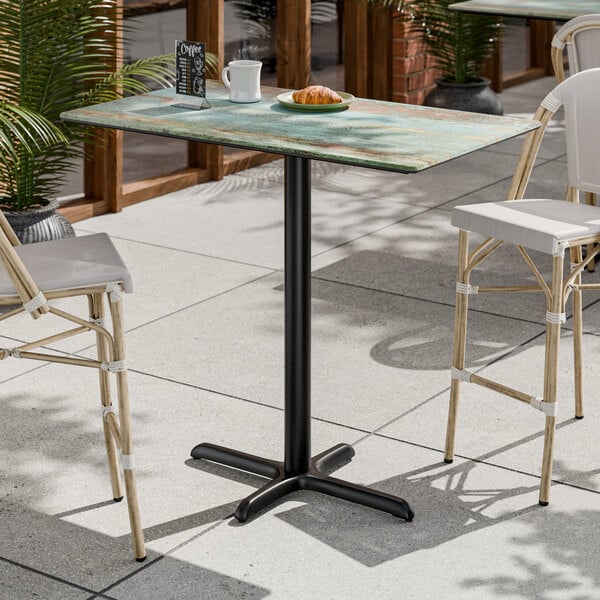 A rectangular bar height table with a textured canyon painted faux metal finish and a black cross base plate.