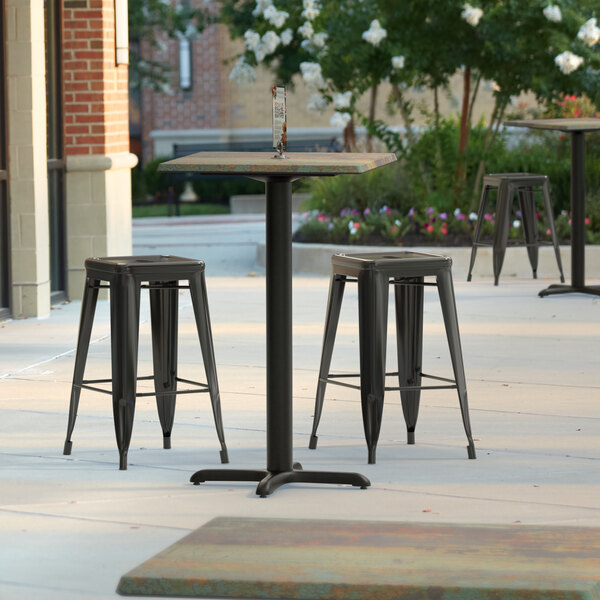 A Lancaster Table & Seating square counter height table with textured metal finish and cross base plate and three stools on a patio.