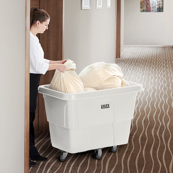 A woman pushing a large white Lavex cube truck with a white bag inside.