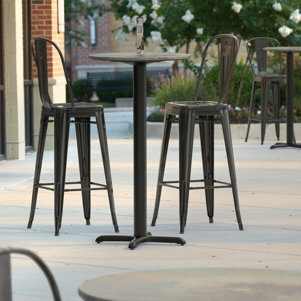 A Lancaster Table & Seating round bar height table and chairs on an outdoor patio.