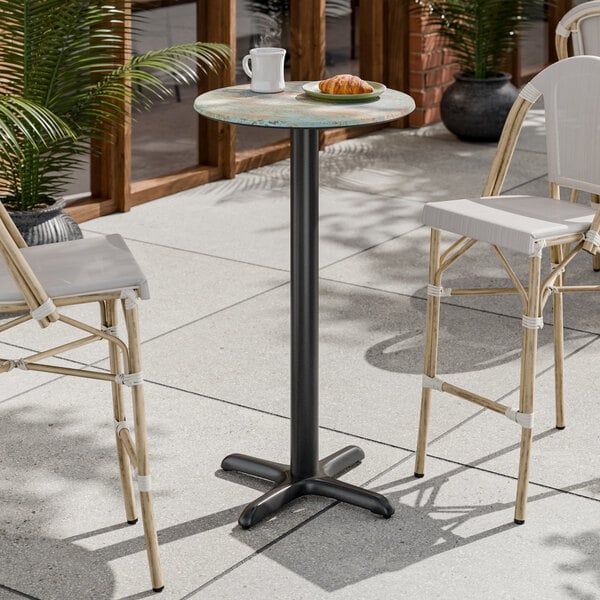 A round bar height table with a textured faux metal finish and a cross base plate.