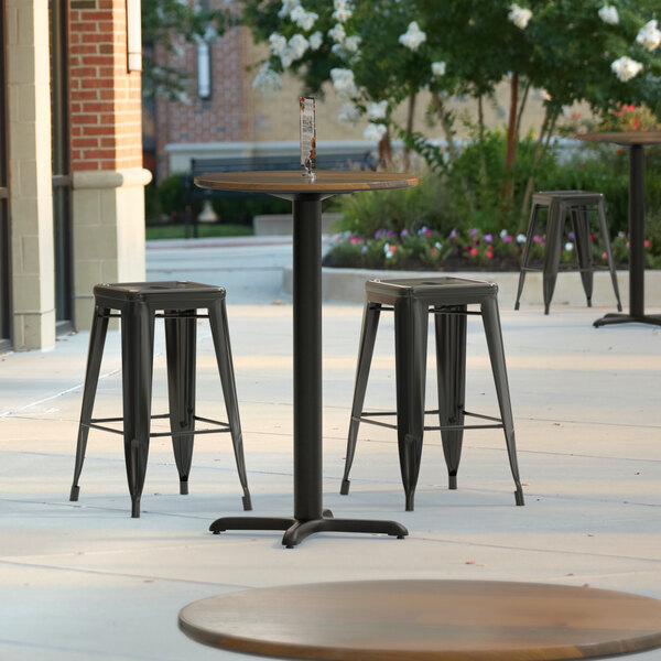 A Lancaster Table & Seating round counter height table with a textured farmhouse finish and cross base plate on an outdoor patio.