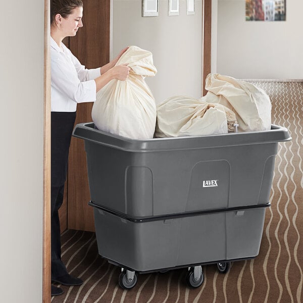 A woman pushing a large grey bag in a Lavex gray cube truck with wheels.