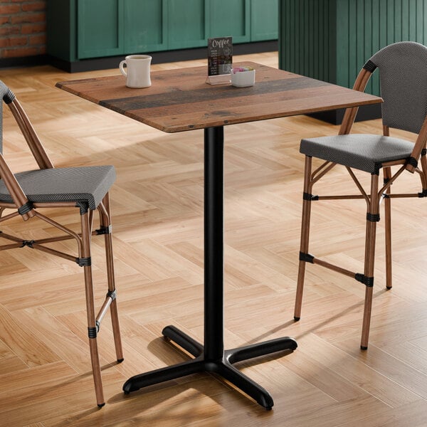 A square bar height table with a textured farmhouse finish and a black cross base plate.
