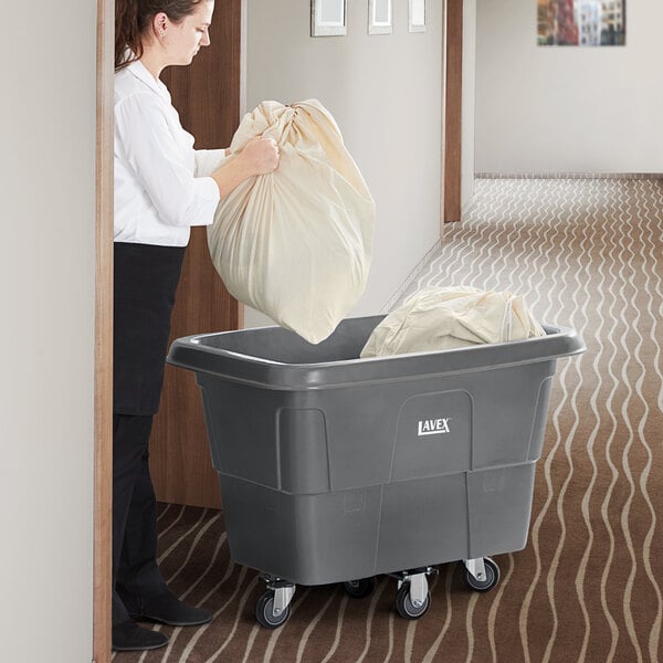 A woman using a Lavex gray cube truck to hold a large white bag.