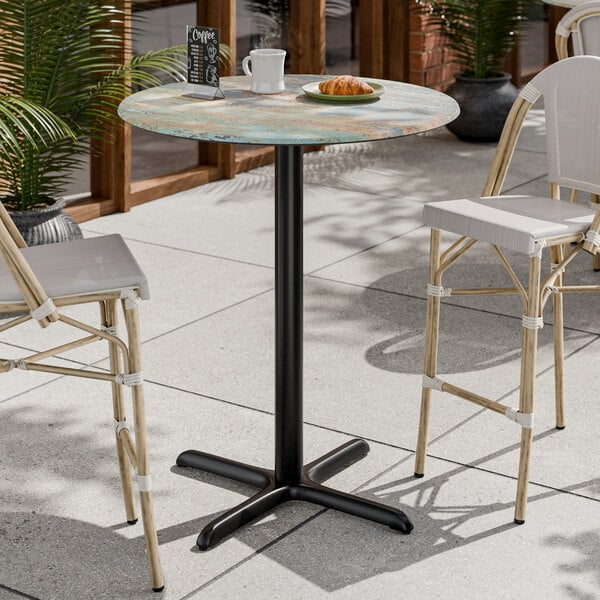 A round bar height table with a textured canyon painted faux metal finish and a black cross base plate.