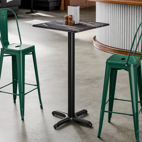 A square bar height table with a smooth dark finish and a black cross base plate.