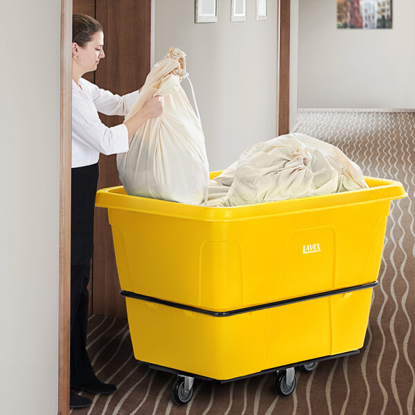 A woman using a Lavex yellow cube truck to hold a large bag.