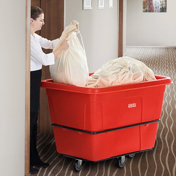 A woman using a Lavex red cube truck to hold a large white bag.