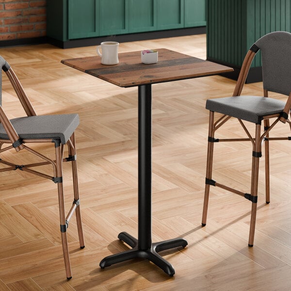 A square bar height table with a textured farmhouse finish and a black cross base plate.