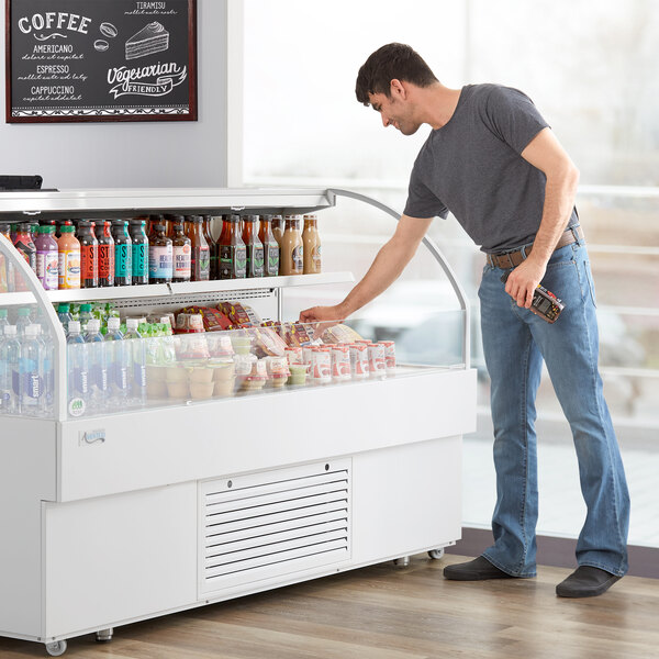 A man standing next to an Avantco white horizontal air curtain merchandiser.